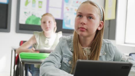 video of attentive caucasian schoolgirl sitting at desk, listening and smiling in class, copy space