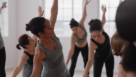 beautiful mixed race yoga woman practicing traingle pose meditation with group of multiracial women enjoying healthy lifestyle exercising in fitness studio at sunrise
