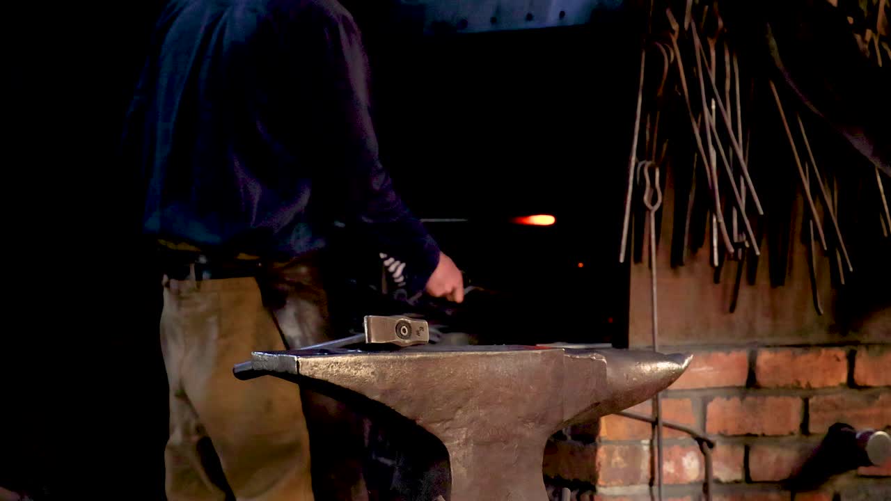 un herrero da forma al metal en un yunque en un taller con poca luz, destacando la artesanía tradicional y el trabajo enfocado