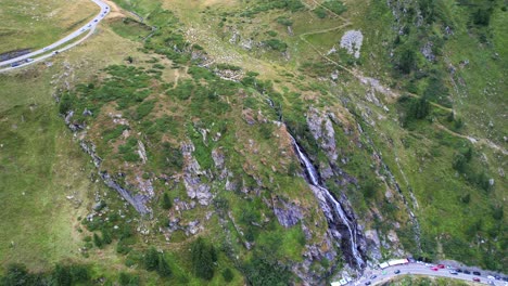 la cascada en cascada corta la pendiente rocosa en la salida en la carretera serpentina de transfagarasan, pedestal panorámico aéreo