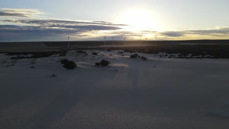 Drohnenluftaufnahme-In-Der-Nähe-Von-Windmühlen,-Die-Während-Eines-Sonnenaufgangs-Mit-Sanddünen-Nach-Links-Schwenken