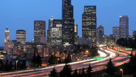 A-Medida-Que-La-Hora-Dorada-Se-Oscurece-En-La-Noche,-El-Tráfico-Acelerado-Se-Difumina-En-Rayas-De-Luz-Ante-Un-Horizonte-Iluminado-De-Seattle-1