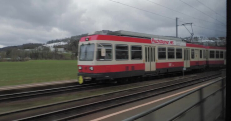 View of red trains through the window seat of a train