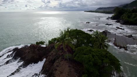 órbita-Aérea-De-La-Costa-Rocosa-Cubierta-De-Vegetación-Y-Espumosas-Olas-De-Mar-Turquesa-En-La-Playa-Dominicalito,-Costa-Rica