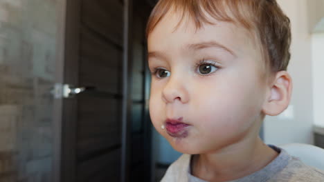 beautiful baby boy eating porridge from spoon. toddler picks a berry and puts it into his mouth. close up.