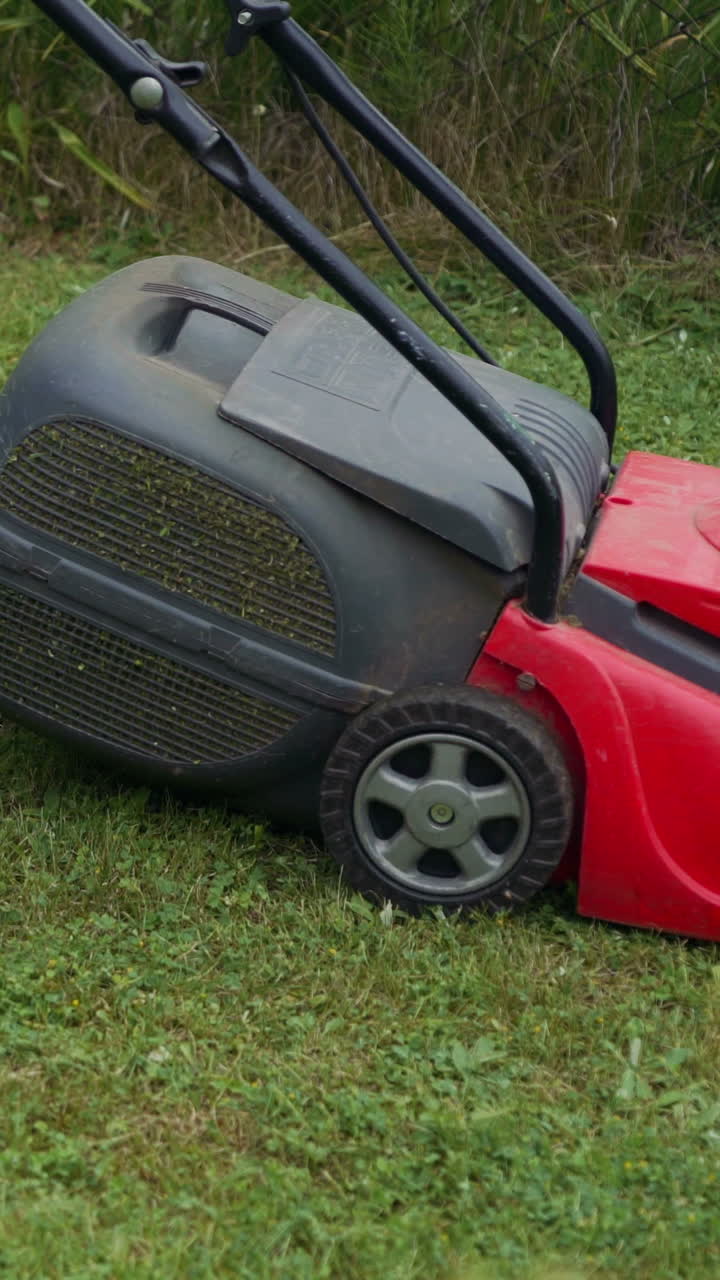 Barefoot young girl mowing grass with a lawn mower in garden. Bare female feet walking behind lawn mower in back yard. Vertical video