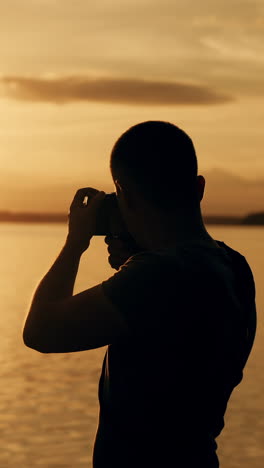 silhouette of photographer taking photos in the river at sunset time.. vertical video