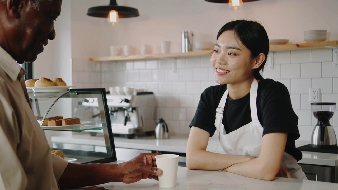 Reaching customer collecting takeaway cup at cafe counter, smiling barista in apron watching