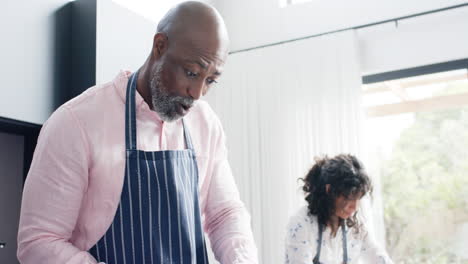 Happy-biracial-couple-wearing-aprons-and-cutting-fresh-bread-in-kitchen,-slow-motion