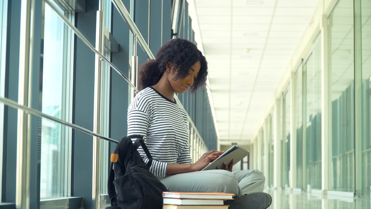 African american woman student sitting on the floor use a tablet in the university. New modern fully functional education facility. Concept of online education