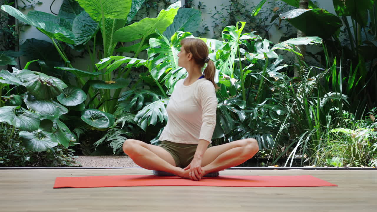 Mulher praticando torção de yoga sentada no tapete em estúdio verde.