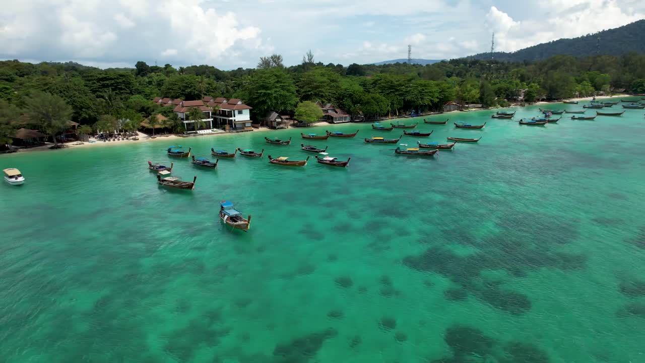 isla koh lipe tailandia, con barcos de cola larga anclados en aguas azules tropicales frente a la costa - rotación aérea a la izquierda