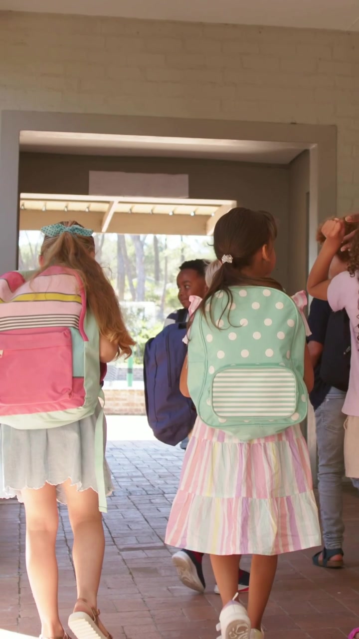 Three students raising hands then stepping through passage backpacks adjusting heading schoolyard