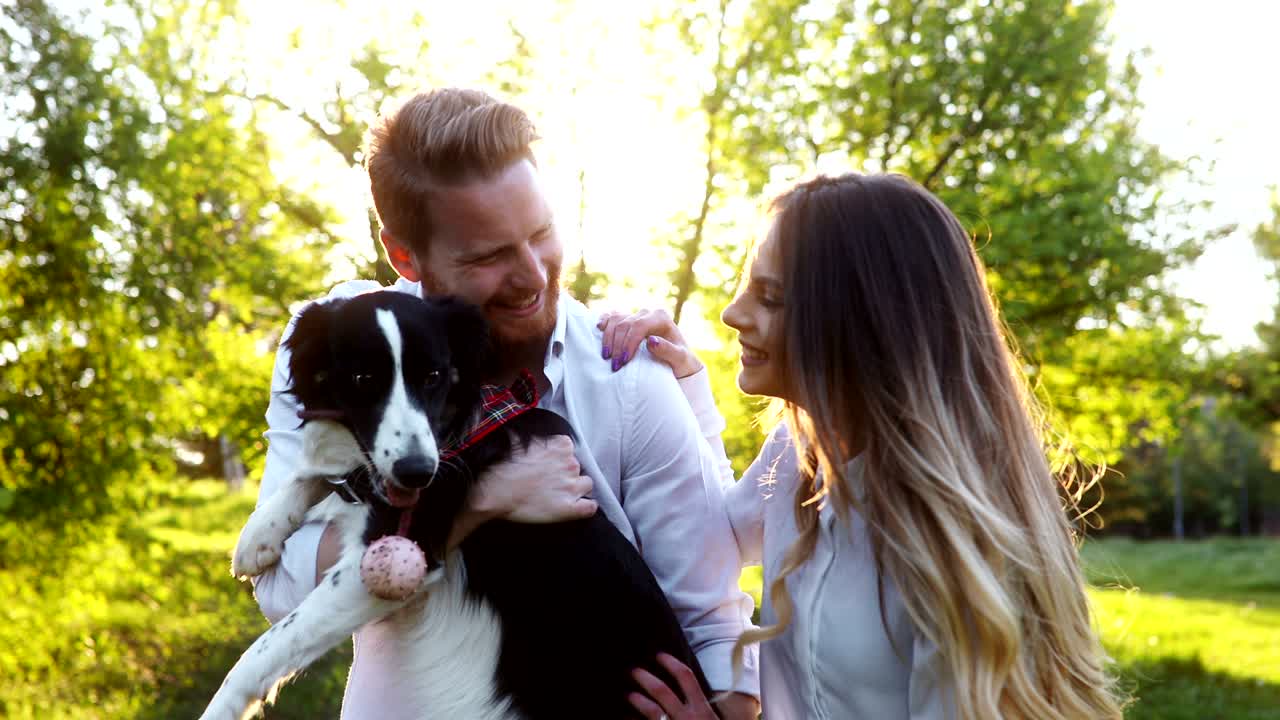 pareja romántica enamorada paseando perros en la naturaleza y sonriendo