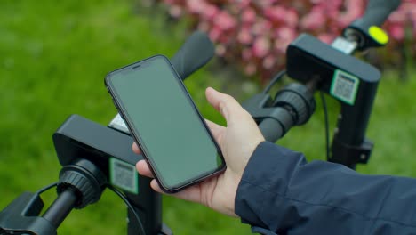 young man paying for electric scooter use app with green mock-up screen smartphone. green screen smartphone.