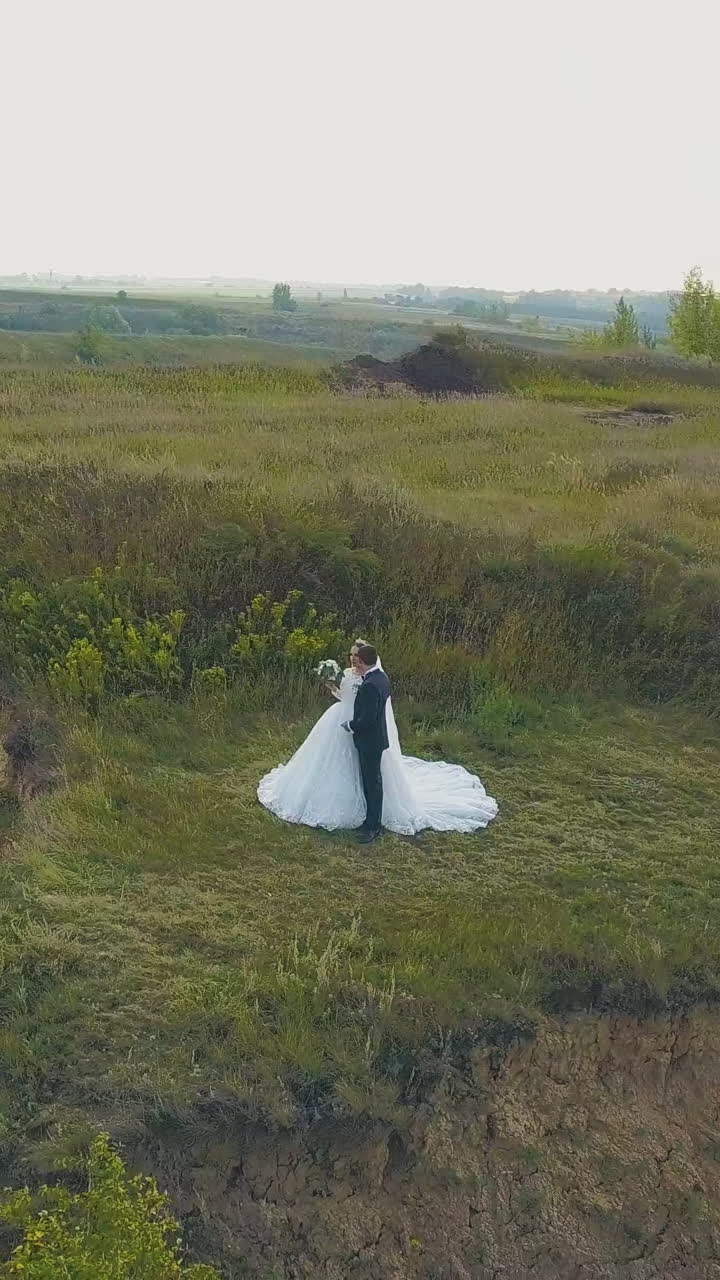 happy young couple kisses on high steep riverbank near large green field on sunny day upper view
