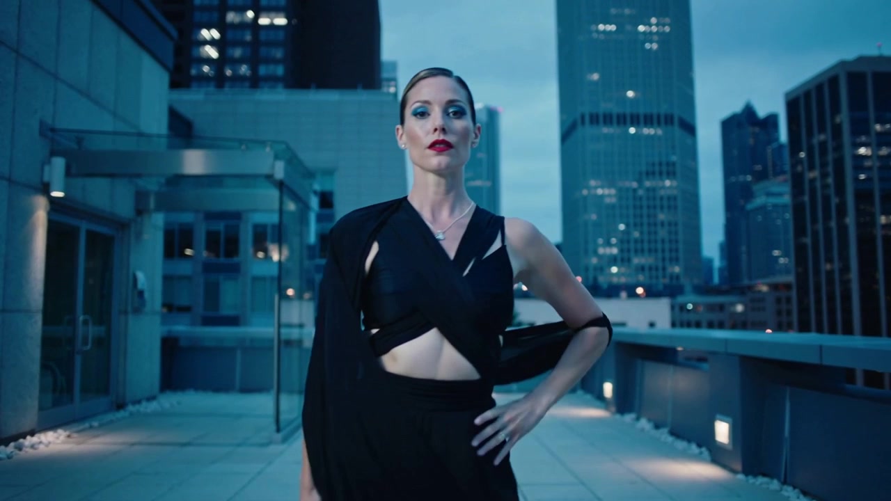 Reacting to camera, woman black outfit rotating, stepping forward, posing on roof terrace with wrap