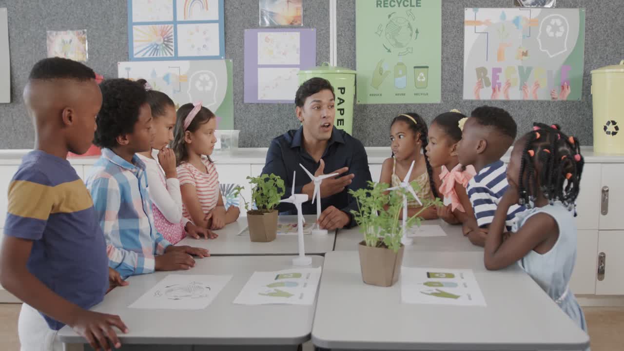 Diverse male teacher and children with wind turbines in elementary school ecology class, slow motion