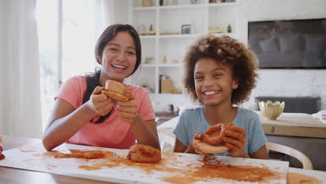 two pre-teen girls laughing and showing their modelling clay creations to camera, front view