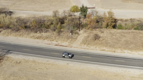 Aerial-forward-scenic-shot-of-metallic-gray-four-wheeler-moving-in-semi-arid-desert-featuring-wide-view-of-nature