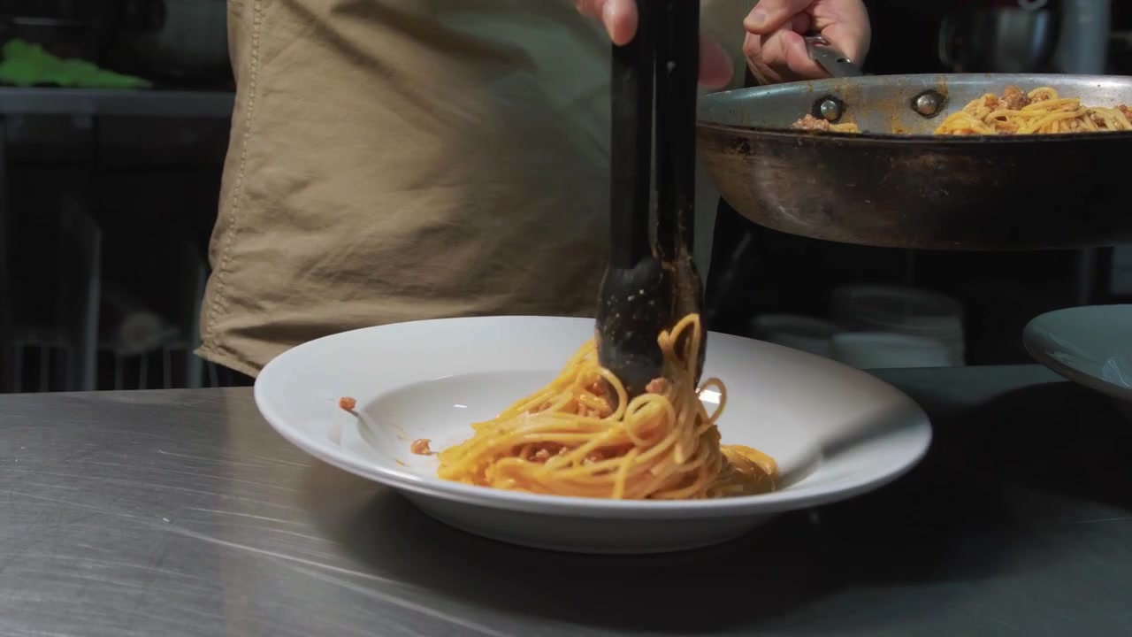 Uno chef serve pasta su un piatto bianco. Versa gli spaghetti alla carbonara cotti, li impiattata e li serve ai clienti.