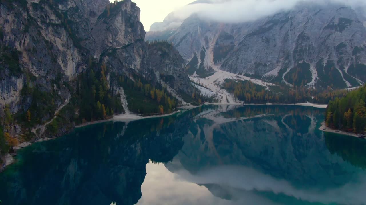 Drone shot of boats on Lago di Braies still as the camera tilts up revealing mountains in the distance.