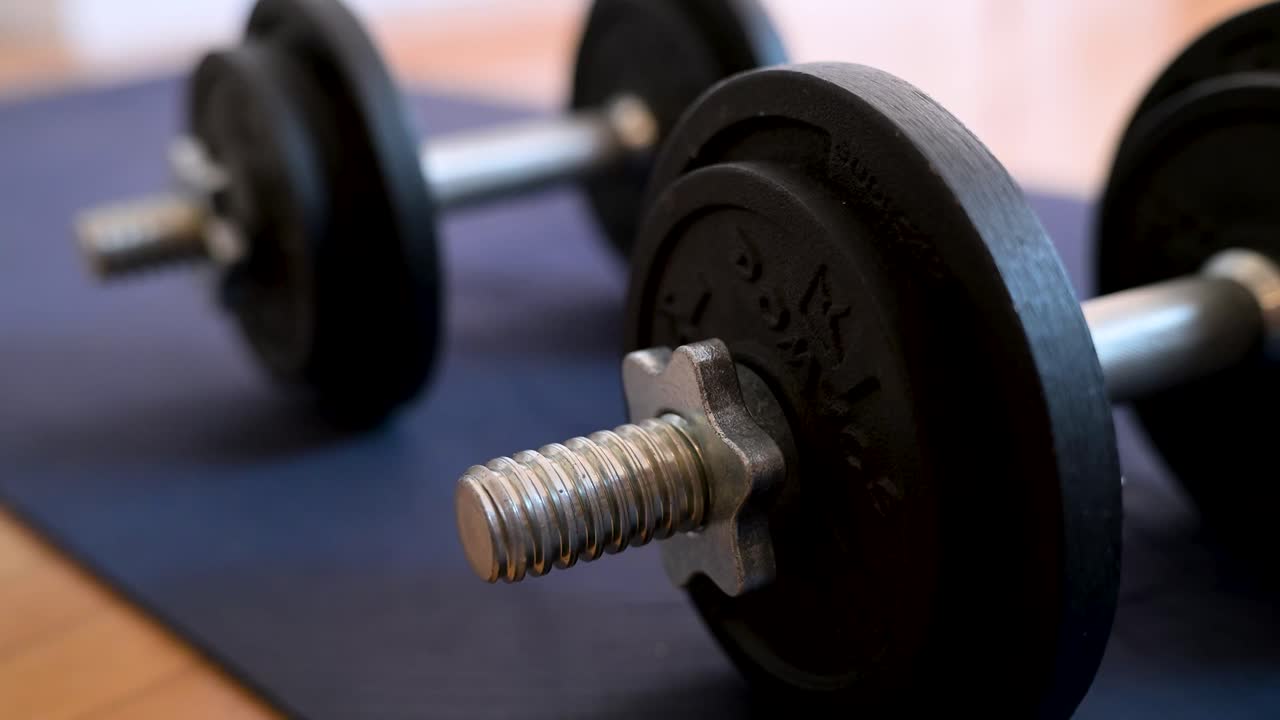 Dumbbells are laid out on a yoga mat, ready for a weightlifting session. A detailed close-up of free weights and equipment for a fitness and bodybuilding home workout