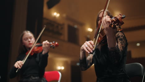 two female violinists are playing music on scene of old opera house orchestra in theater