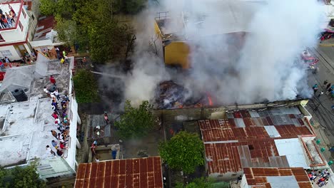 Aerial-drone-view-of-grey-smoke-rising,-while-firefighters-fight-a-raging-building-fire-in-a-city