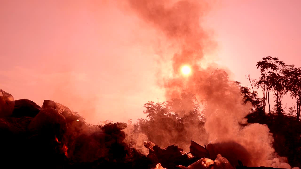fuego en cámara lenta quemando bolsa de basura al amanecer fondo oscuro. humo blanco flotando a la contaminación del aire y el entorno peligroso. la basura es desecho de la comunidad. hace efecto invernadero de la tierra.