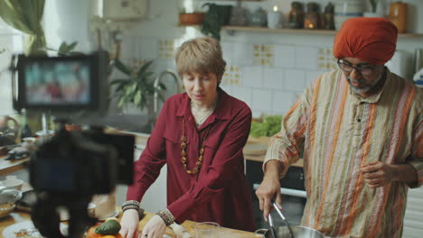 senior indian chef filming culinary show with female co-host in kitchen