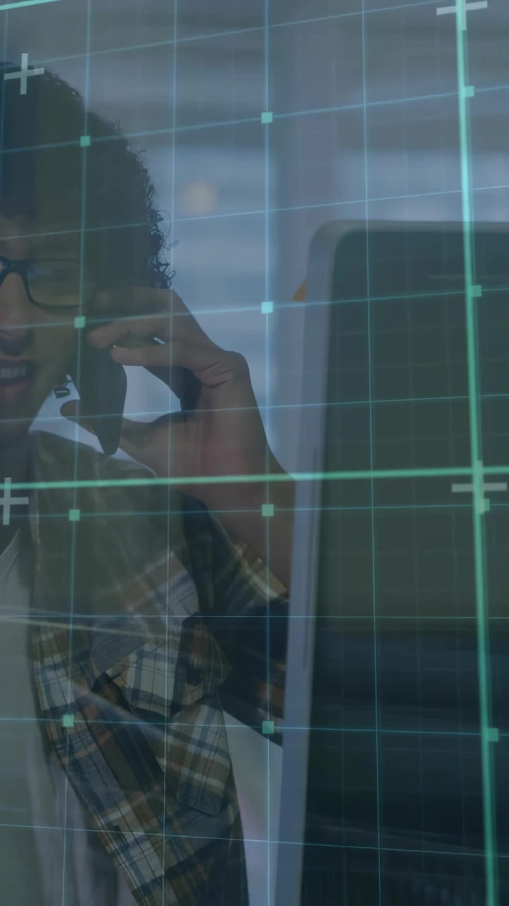 Vertical video: Tech man taking call at desk checking screen while digital grid guiding work