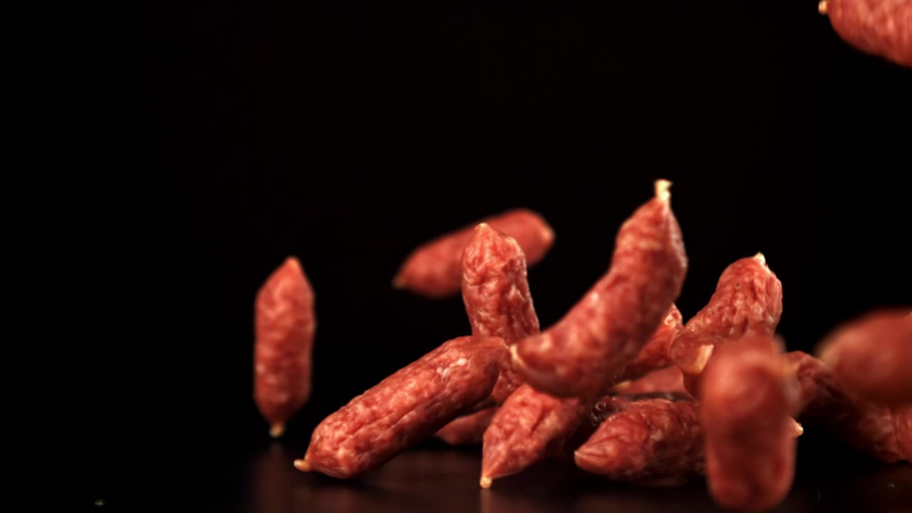 Mini salsicce di salame rosse che cadono al rallentatore su sfondo nero.