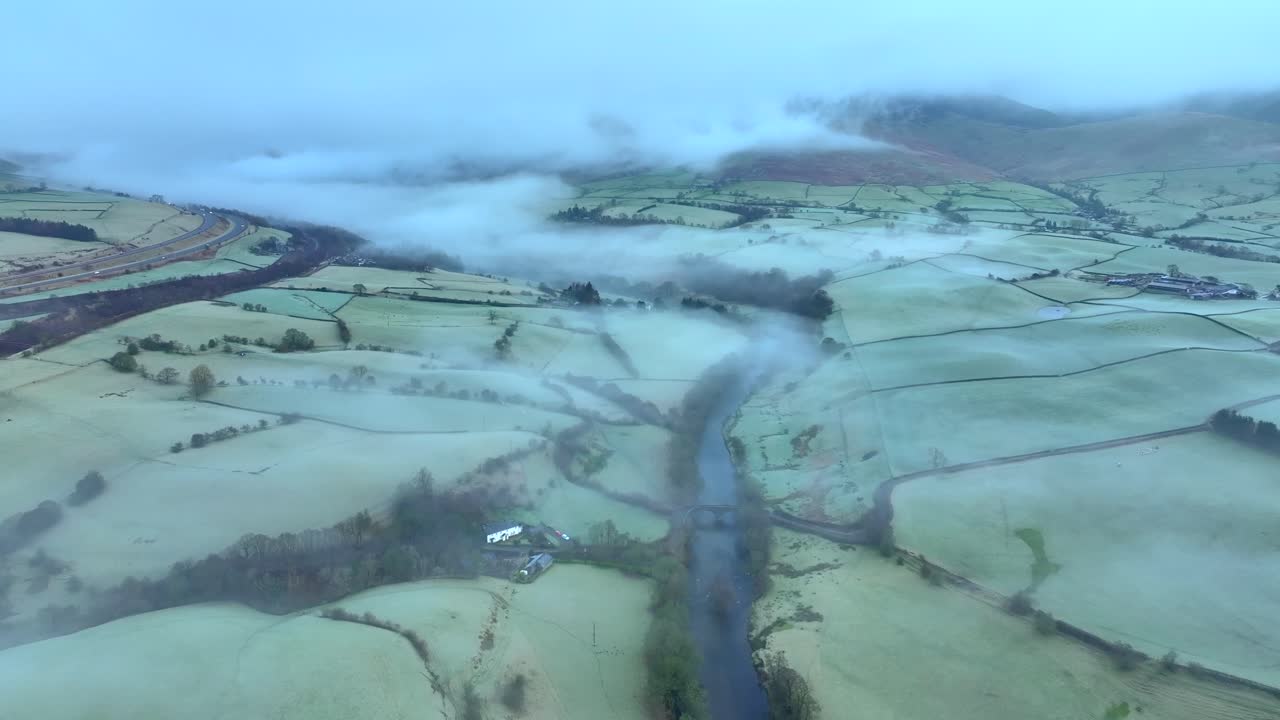 un río serpenteante envuelto en niebla entre campos verdes y cubiertos de helada al amanecer en invierno