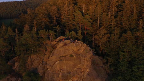 Grupo-De-Adolescentes-En-La-Cornisa-Y-El-Acantilado-De-Una-Enorme-Montaña-Mientras-El-Dron-Vuela-Hacia-Atrás-Revelando-Toda-La-Cordillera-En-El-Bosque-Negro,-Alemania-En-4k