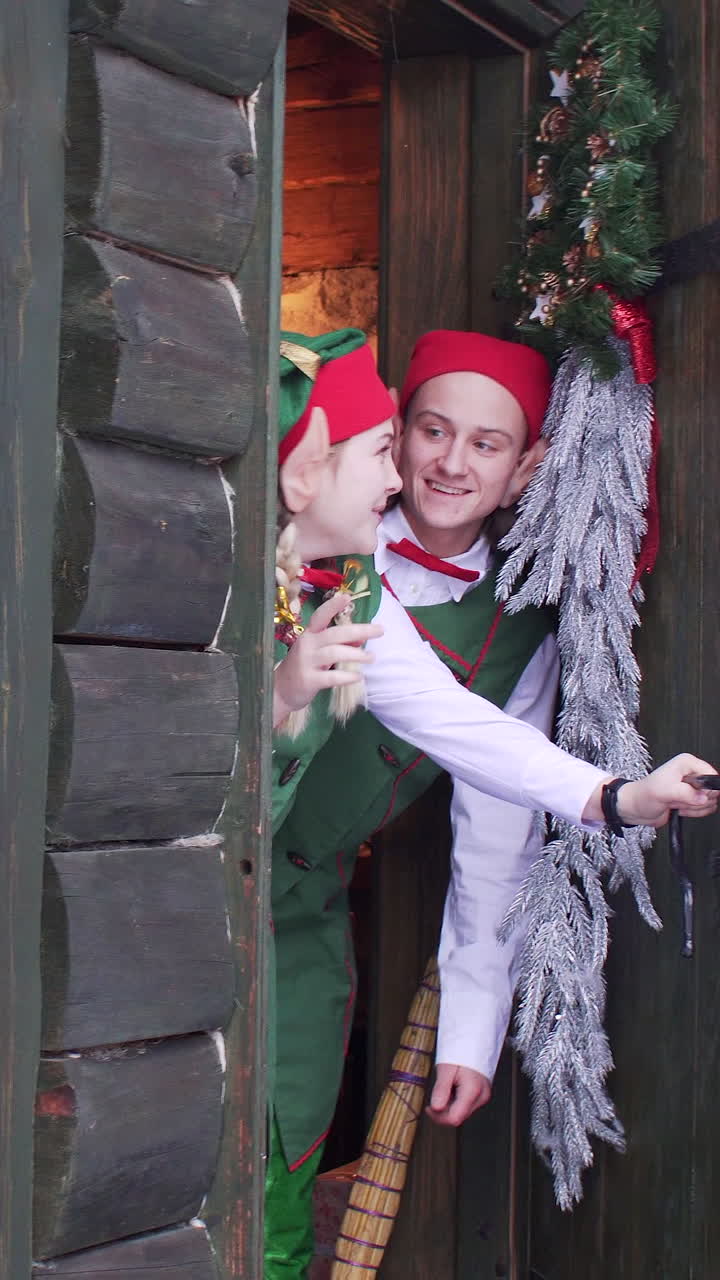 Elves peep out from behind a wooden door of santa claus residence. Vertical video
