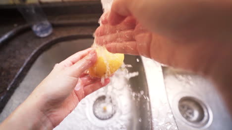 Weibliche-Hände-Waschen-Eine-Kartoffel-Unter-Wasser-Aus-Einem-Küchenhahn-In-Zeitlupe