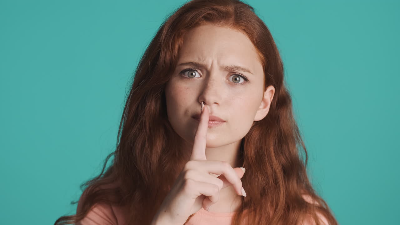 Redheaded girl in front of camera on turquoise background.