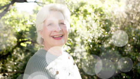 Animación-De-Puntos-De-Luz-Y-árboles-Sobre-Una-Mujer-Caucásica-Mayor-Sonriente-En-El-Jardín