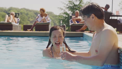 Amorosa-Pareja-Madura-Relajándose-En-La-Piscina-En-Vacaciones-De-Verano-Celebrando-Bebiendo-Champán