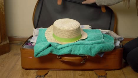 woman packing straw hat into suitcase wide shot