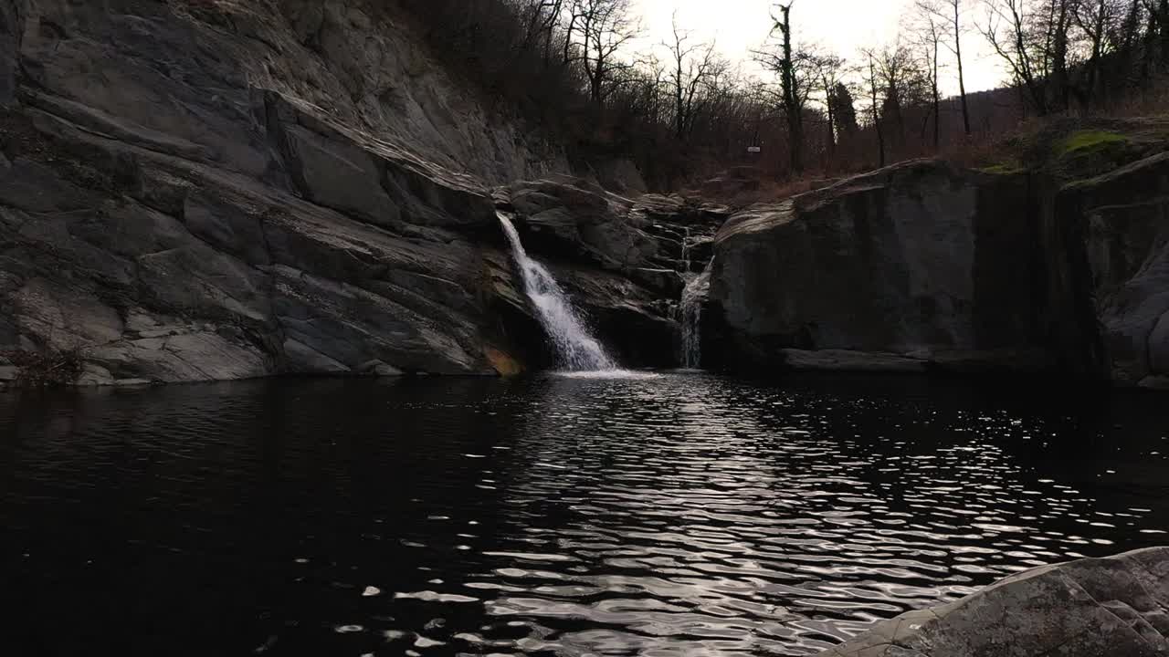 Volo stazionario del drone sopra alcune pietre e una cascata di giorno vicino a una pietra