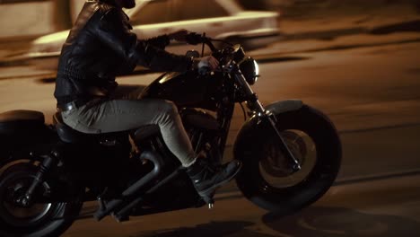 side view of a brutal man riding fast his bike by night city street, close up of wheels