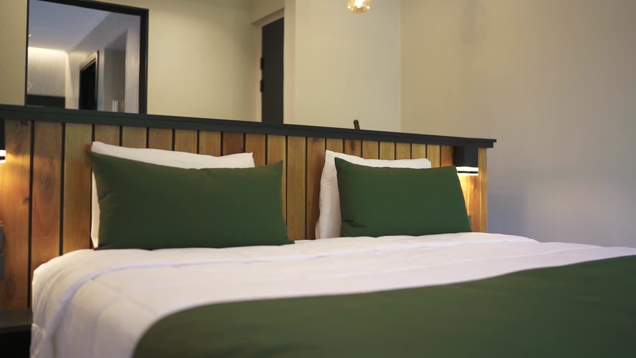 A stylish hotel room with a comfortable bed with green and wood accents, modern decor, and ambient lighting for relaxation, establishing pan right