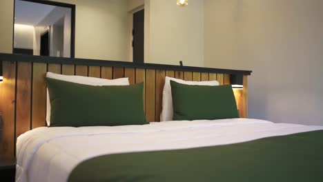 a stylish hotel room with a comfortable bed with green and wood accents, modern decor, and ambient lighting for relaxation, establishing pan right