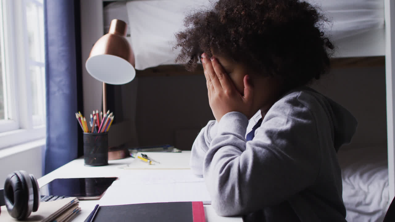 Ragazza meticcia seduta alla scrivania che si copre gli occhi