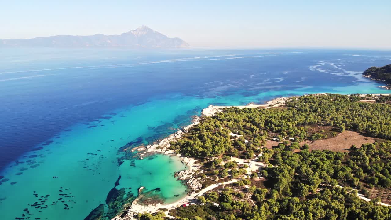 Aerial drone view of the Aegean sea rocky coast with blue transparent water, multiple greenery, mountain on the background. Greece