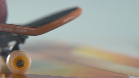 a hyper close-up macro detailed shot of a mini skateboard, tiny white wheels, riding fingerboard from right to left, finger slide, professional lighting, dreamy cinematic 4k video