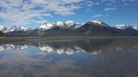 o drone sobe acima das águas brilhantes do braço de turnagain, no alasca, com majestosos picos cobertos de neve das montanhas chugach, na península de kenai, ao fundo.