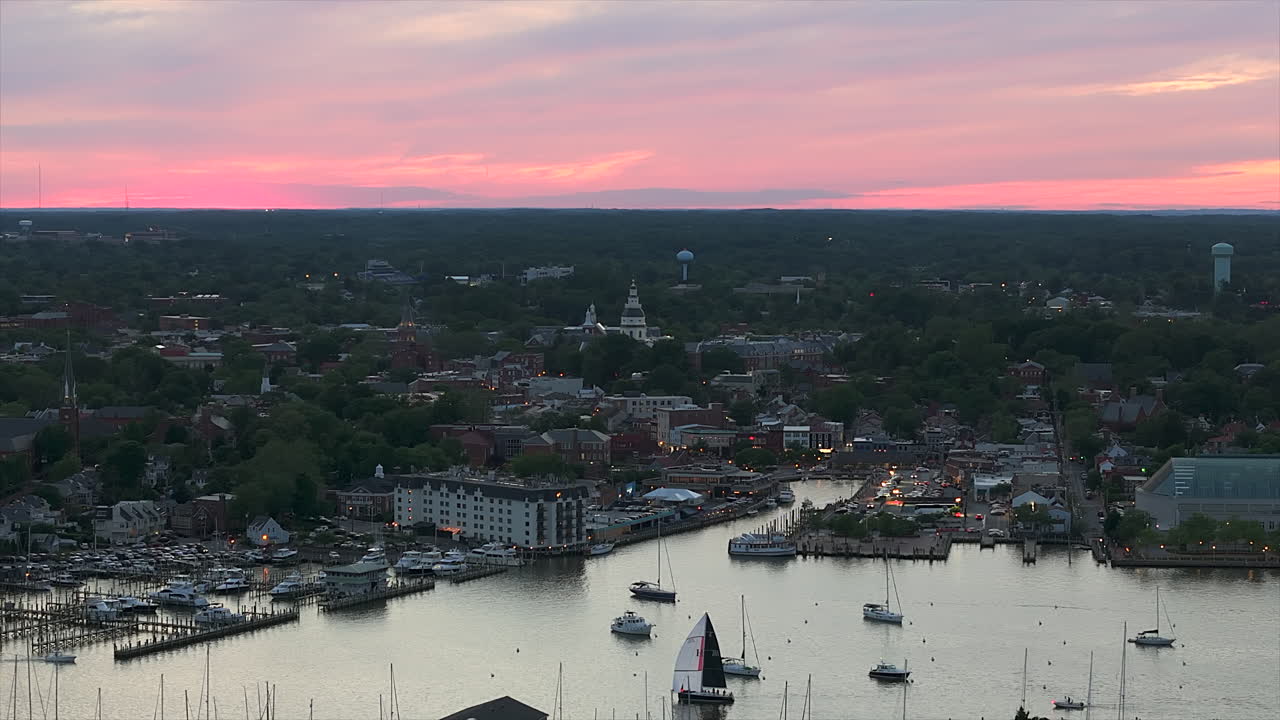 Flyvende mod Annapolis, Marylands havn mens sejlbåde glider på vandet under en blød, lyserød himmel - droneoptagelse